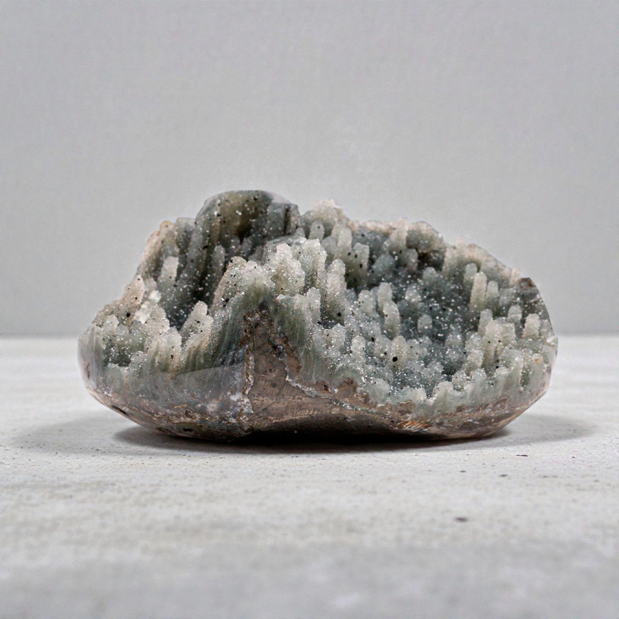 Small natural crystal geode displaying a grey quartz crystal cluster with fine druzy texture, organic chalcedony edges, and a raw mineral silhouette suited for luxury neutral decor.